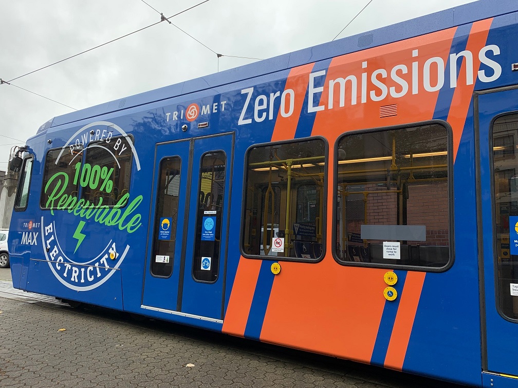 A Blue and Orange TriMet MAX train with the words "100% renewable electricity" "Zero Emissions"