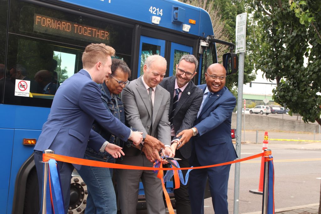 From left, West Linn Mayor Rory Bialostosky, Oregon City Mayor Denyse McGriff, Clackamas County Commissioner Paul Savas, Lake Oswego Mayor Joe Buck and TriMet General Manager Sam Desue Jr. cut an orange ribbon in front of a TriMet bus displaying the message "Forward Together."